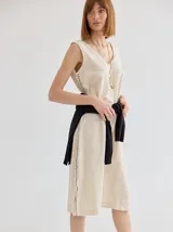 Vestido color crudo, de corte recto y largo a la rodilla, sin mangas y con escote en V. Presenta detalle de costura en zigzag a lo largo de los laterales.