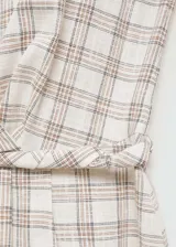 Vestido midi a cuadros color beige con líneas marrones, de corte evasé, sin mangas y con cuello redondo. Presenta un detalle cruzado en la cintura.