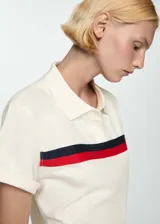 Polo crop color crema con cuello clásico, cierre de botones parcial y mangas cortas con dobladillo. Presenta una franja horizontal con rayas rojas y azul marino en el pecho.