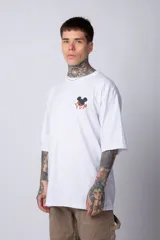 Remera blanca de algodón de corte oversize con mangas cortas y cuello redondo. Presenta un pequeño estampado en el frente con la figura de Mickey Mouse y caracteres orientales.
