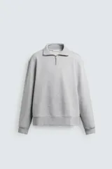 Sudadera gris de corte regular, con cuello alto y cierre frontal de cremallera metálica. Manga larga y terminaciones en rib.