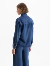 Camisa azul de manga larga confeccionada en 100% Tencel, con lazo en el cuello y acceso mediante broches dorados en la cartera delantera.