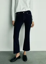 Pantalón de jean azul oscuro, de tiro alto, corte ajustado en la cadera y muslos, y acampanado a partir de la rodilla. Largo cropped.