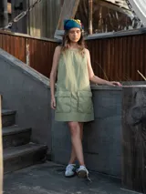 Vestido corto verde oliva, sin mangas, con cuello redondo y dos bolsillos grandes tipo parche en el frente.