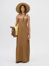 Vestido midi de denim algodón color marrón, con escote recto y tirantes finos ajustables con lazos. El corte es suelto y termina con un ruedo con semi-volado.