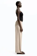Pantalón de corte holgado color beige, confeccionado en sarga de mezcla de lyocell. Modelo de tiro alto con cintura fruncida, cierre decorativo y bolsillos laterales discretos. Piernas rectas con pliegues cosidos adelante y raya planchada atrás.