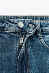 Pantalón de jean gris oscuro, de corte mom fit, tiro alto y largo tobillero. Cuenta con cinco bolsillos, cierre frontal con cremallera y botón.