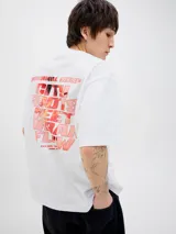 Camiseta blanca de manga corta con cuello redondo, corte holgado y estampado frontal con la frase "City Roots Meet Urban Flow" en color rojo.