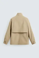 Parka ligera color beige, de corte relaxed fit, confeccionada en tejido técnico repelente al agua. Tiene cuello alto, mangas largas con puños ajustables con botón a presión, bolsillos de solapa en la cadera y cierre frontal con cremallera oculta por solapa con botones a presión.