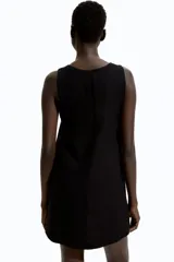 Vestido corto negro sin mangas, de corte evasé, con escote redondo, abertura de cerradura con botón oculto en la nuca y bajo recto. Parcialmente forrado.