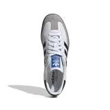 Championes Adidas Samba OG, color blanco con detalles en negro y gris. Diseño clásico de cuero con las tres tiras laterales en contraste y suela de goma marrón.