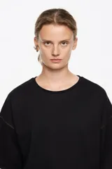 Camiseta negra de corte recto con escote redondo y mangas cortas anchas. Presenta pespuntes a contraste de color marrón claro en las sisas y los bordes de las mangas.