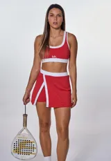 Conjunto deportivo rojo con detalles en blanco, compuesto por un top con logo 'bk.' y una falda-short con abertura lateral.