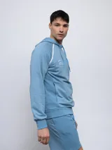 Canguro de felpa color crema con capucha, cordones y logo Umbro bordado en rojo. Presenta ribete rojo en hombros y bolsillo tipo canguro con cierre lateral.