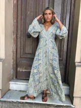 Vestido largo fluido con escote en V y mangas abullonadas 3/4. Presenta un estampado tipo paisley en tonos celeste, beige y gris.