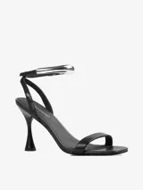Sandalias de tacón negras con tira delgada sobre los dedos y pulsera tobillera con adorno tubular plateado.