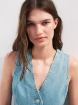 Chaleco de jean celeste con cuello en V, sin mangas, cierre frontal con botones y lazo ajustable en la cintura.