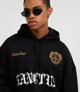 Hoodie negro de corte boxy, con capucha ajustable, bolsillo canguro y detalles bordados en el pecho. Presenta un estampado grande en la parte frontal con tipografía gótica y texto en dorado.