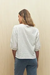 Blusa color crema con diseño calado, escote en V y volados frontales. Tiene mangas 3/4 con puños elastizados y cierre frontal con botones.