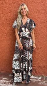 Vestido largo con estampado tipo patchwork en tonos tierra, blanco y azul oscuro. Presenta escote cruzado en V y mangas cortas. La falda es larga y con vuelo.