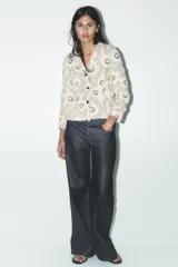 Blazer color crudo con estampado de flores negras, cuello solapa con muescas, manga larga y cierre frontal con botones negros.