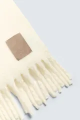 Bufanda color crema confeccionada en tejido con lana y acabado cepillado. Tiene flecos en los extremos.