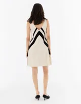 Vestido corto de tela liviana color crema, con escote en V y diseño de patchwork con piezas de tela negra que crean una V.