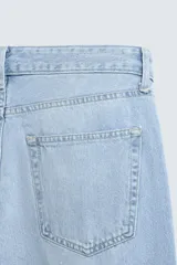 Pantalón de jean celeste de corte flare, con tiro medio, cinco bolsillos, cierre frontal con cremallera y botón, y bajo con acabado irregular.