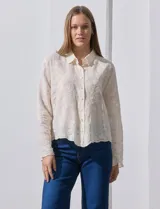 Camisa de manga larga color beige, con bordado tipo broderie, cuello con solapa y abertura central con botones.