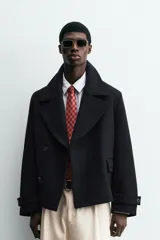 Abrigo corto azul marino de corte relajado, confeccionado en tejido con lana. Tiene cuello con solapas de pico, mangas largas con puños ajustables con trabilla, bolsillos de solapa en la cadera, bolsillo interior, abertura en el centro de la espalda y cierre frontal con botonadura.