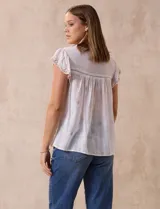 Blusa color marrón claro de algodón con bordados y calados blancos. Tiene cuello a la base, escote en V con lazo de ajuste y mangas cortas amplias.