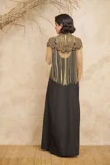 Capa negra con cuello alto y bordados dorados. Presenta flecos largos dorados que caen desde los hombros.