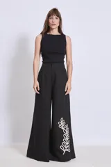 Pantalón negro de corte palazzo con apliques bordados en color crema en la parte inferior de una pierna.
