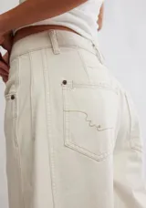 Pantalón de jean color crema, de corte relajado, piernas anchas y tiro medio. Tiene una silueta distinta y un largo hasta los tobillos.