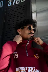 Buzo de algodón color bordó, estilo universitario, con cierre medio frontal y cuello alto. Estampado frontal con el texto "Since 19" y un ancla con laureles en amarillo y blanco.