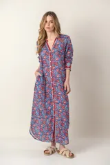 Vestido largo con estampado floral en tonos rosa y verde sobre fondo blanco. Tiene cuello con volantes, cierre frontal con botones y mangas largas con puños elásticos.