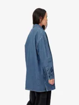 Camisa de denim azul con corte oversize y un bolsillo frontal, de estilo urbano.