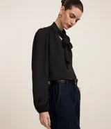 Blusa negra de crepé con cuello con lazo, mangas largas y pliegues en los hombros.