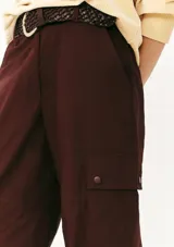 Pantalón cargo color borgoña, de corte recto, con bolsillos laterales con solapa y cinturón trenzado marrón.