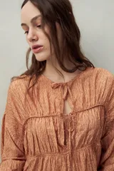Blusa estampada de caída fluida con cuello redondo y lazos frontales, diseño con cortes horizontales y frunces, mangas largas con puños elastizados.