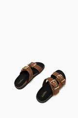Sandalias planas color tostado con dos tiras anchas sobre el empeine, cada una ajustable con hebillas metálicas doradas.