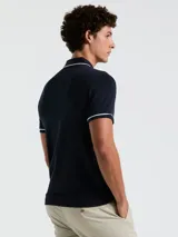 Polo de piqué azul marino de manga corta con vivos blancos en cuello y mangas, tapeta con botones y bolsillo en el pecho con logo bordado.