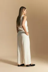 Pantalón de vestir de tiro alto, color beige claro con finas rayas verticales oscuras. Es de corte ancho y largo, con un lazo de tela a juego anudado en la cintura. Se combina con un top sin mangas del mismo tejido y color.