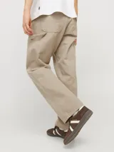 Pantalón jean color arena, de corte amplio, tiro alto y diseño de carpintero con múltiples bolsillos.