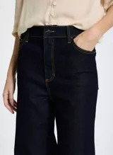 Pantalón de jean de tiro alto, color azul oscuro, con corte flare y costuras en color ocre.