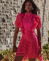 Vestido corto de encaje color fucsia, con cuello alto, mangas cortas con volantes y falda asimétrica.