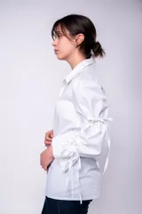 Camisa blanca de mangas largas abullonadas con lazos en los puños y cuello clásico. Cierre frontal con botones.