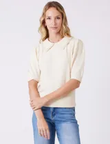 Buzo tejido color beige, marca Nanette, con cuello a la base y solapa decorada con apliques de perlas. Tiene manga corta con puño y ruedo acanalado.