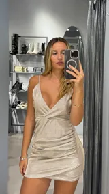 Vestido corto dorado con lurex, escote en V y breteles finos. Diseño drapeado con frunce lateral.