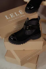 Botín negro de cuero con elástico lateral, puntera charolada y hebilla decorativa.